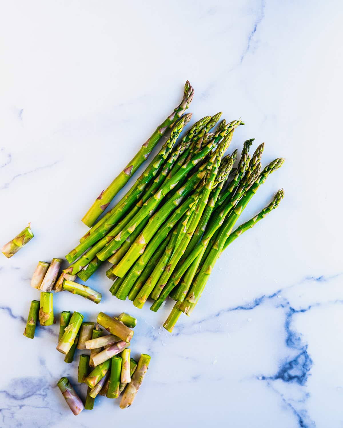 Asparagus spears lined up on a marble counter with the ends trimmed off