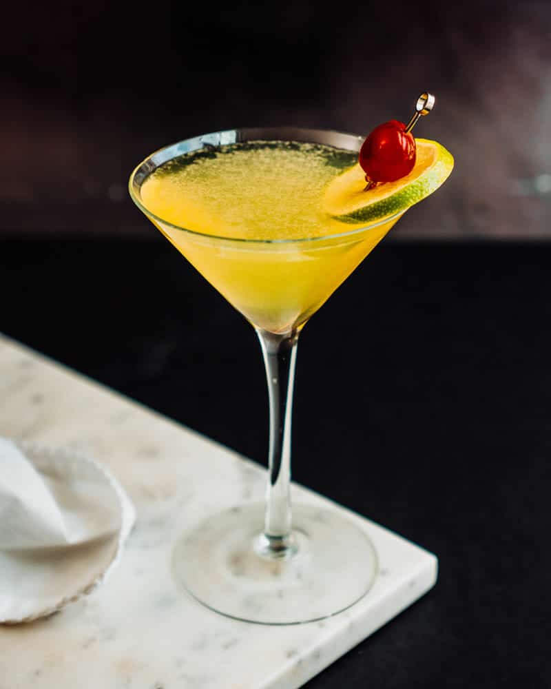 Yellow Bird Cocktail in a long-stemmed glass and garnished with a lime and cherry.