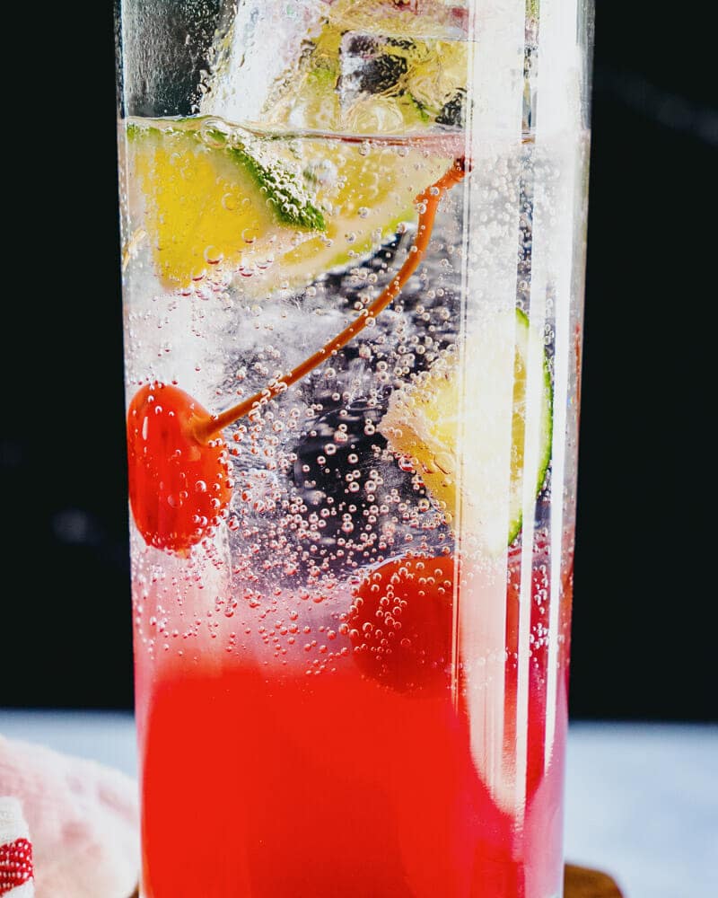 A cherry lime rickey served in a highball glass, garnished with cherries and lime