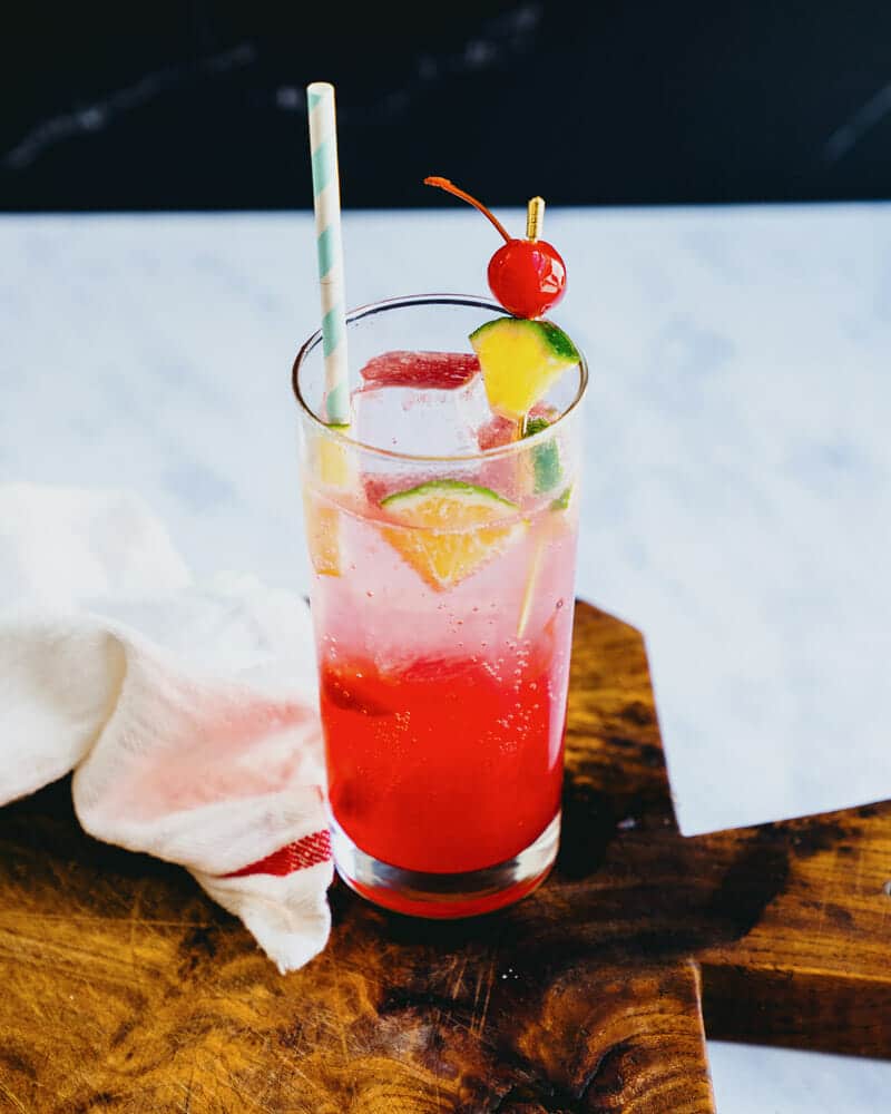 A cherry lime rickey served in a highball glass, garnished with cherries and lime, and served with a colorful straw