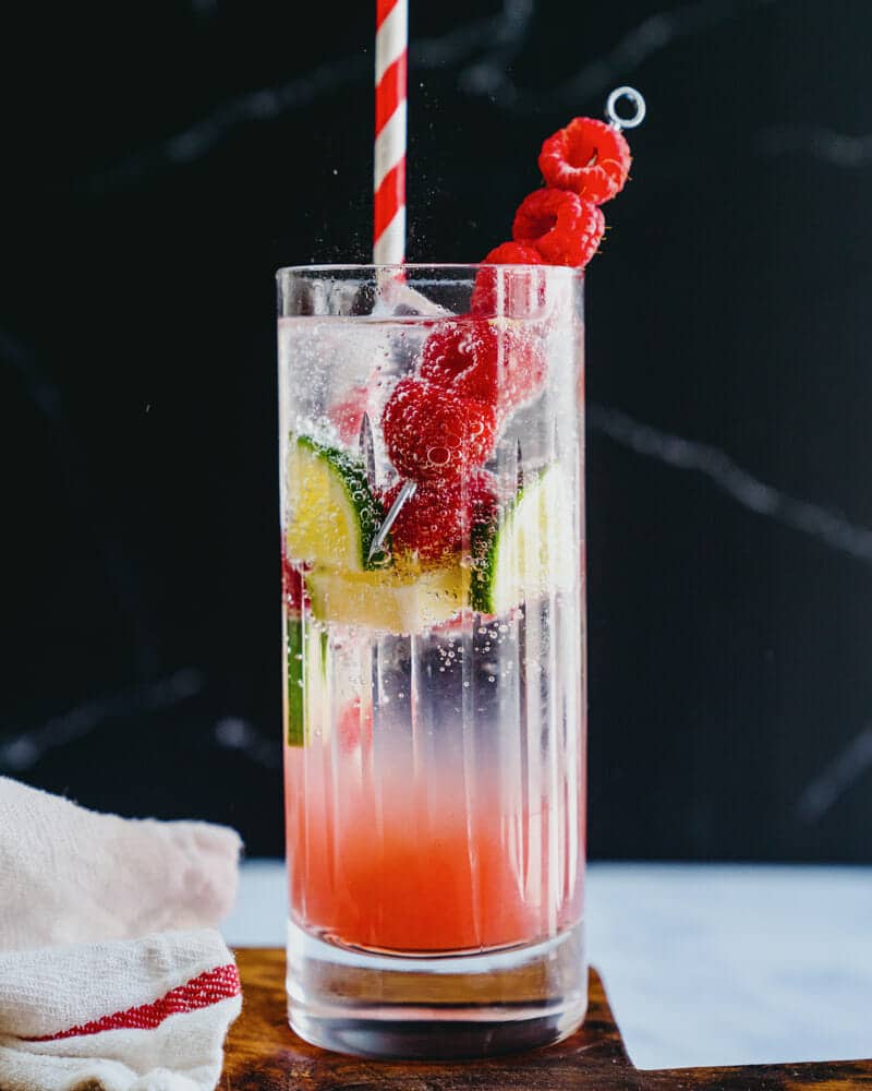 A raspberry lime rickey served in a highball glass, garnished with raspberries and lime, and served with a colorful straw