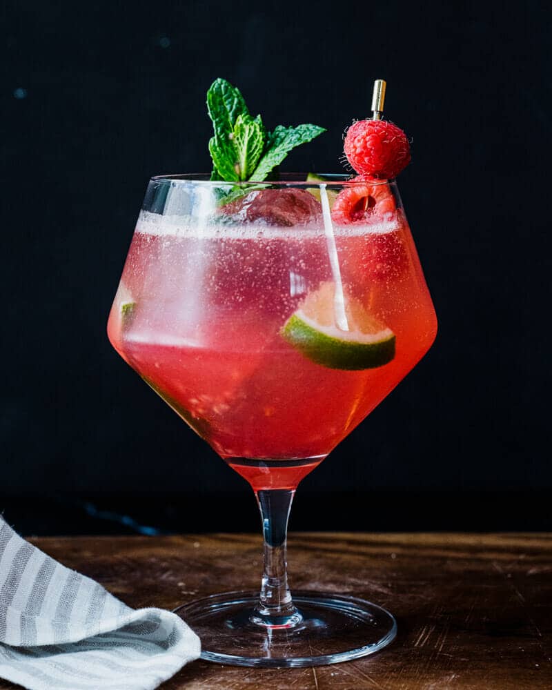 Raspberry mojito in a shaped glass and garnished with raspberries, mint, and lime