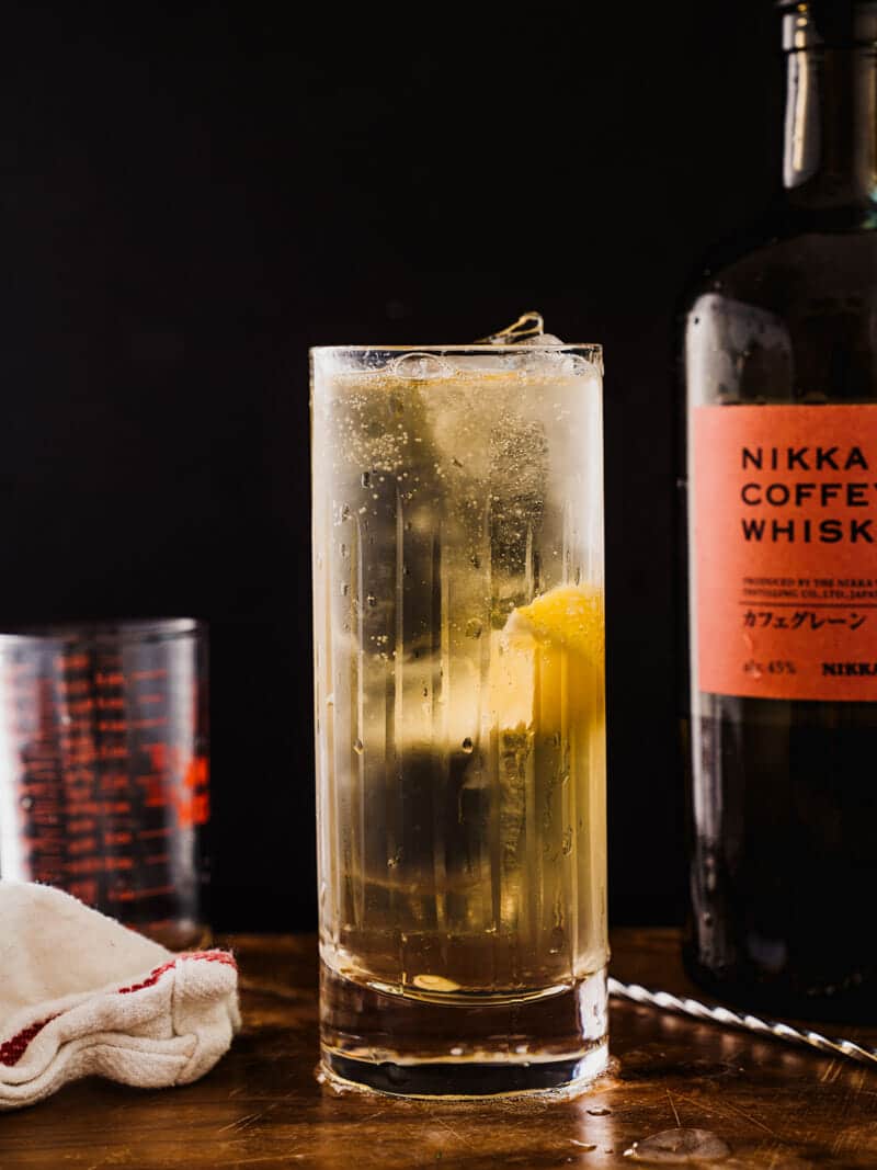 Japanese highball in a tall glass, garnished with a lemon, and sitting next to a bottle of Nikka Coffey Grain Whisky