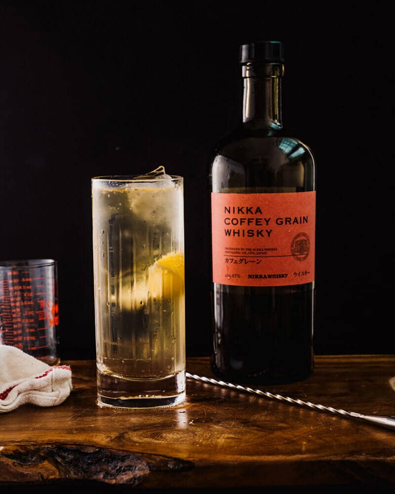 Japanese highball in a tall glass, garnished with a lemon, and sitting next to a bottle of Nikka Coffey Grain Whisky