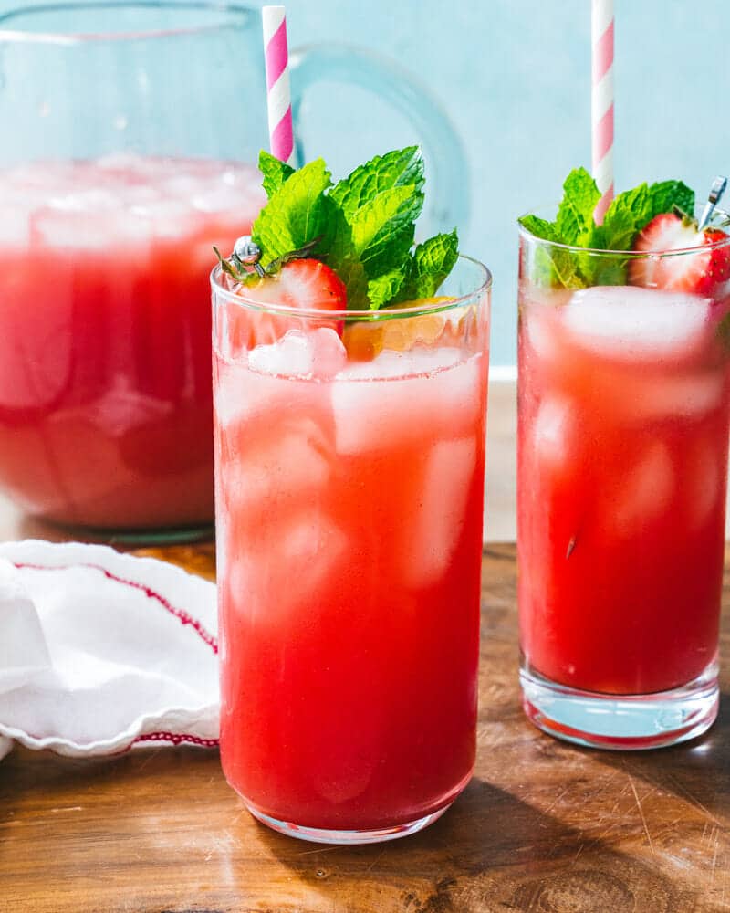 2 Glasses of strawberry water in tall glasses with ice, colorful straws, and garnished with strawberries