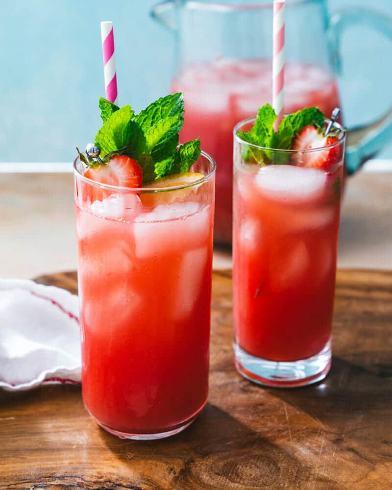 Two tall glasses of strawberry water with ice, and garnished with strawberries
