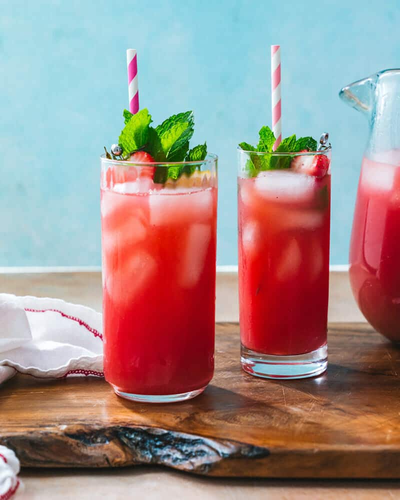 Two tall glasses of strawberry water with ice, and garnished with strawberries