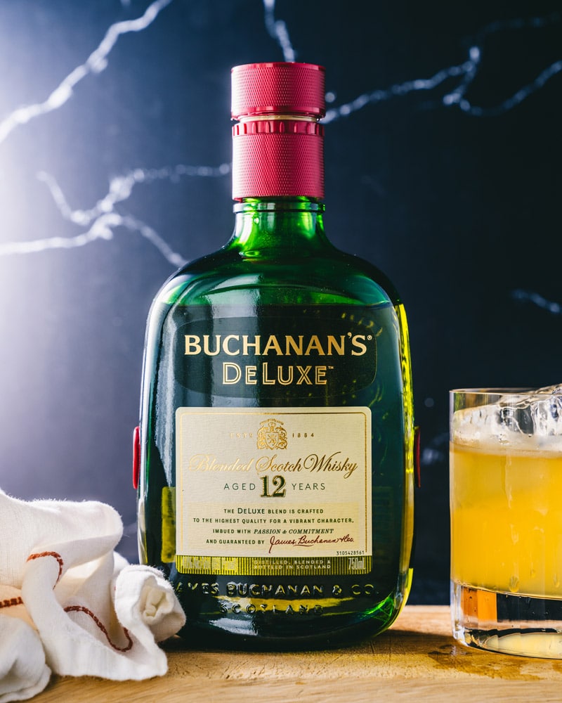 Bottle of Buchanan's DeLuxe Scotch Whisky sitting next to a Buchanan sour in a glass