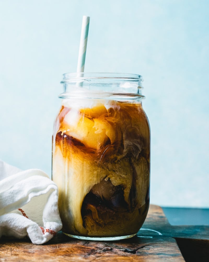 A mason jar glass with coffee and milk over ice, with a straw.