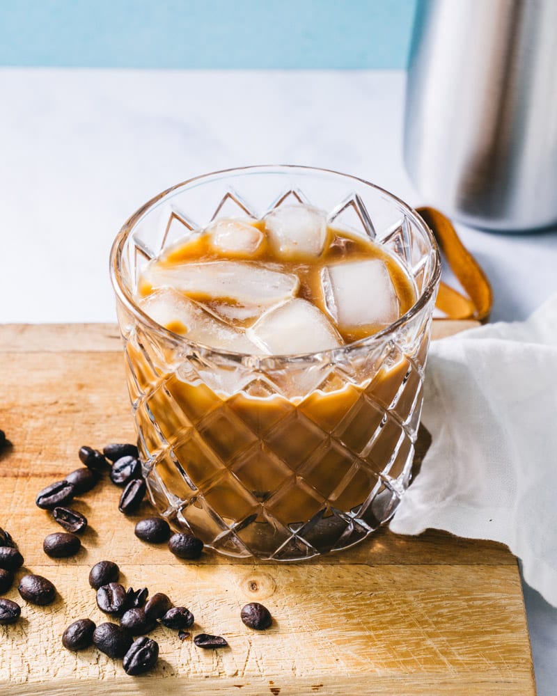 Iced espresso in a textured glass with coffee beans scattered on the table next to it