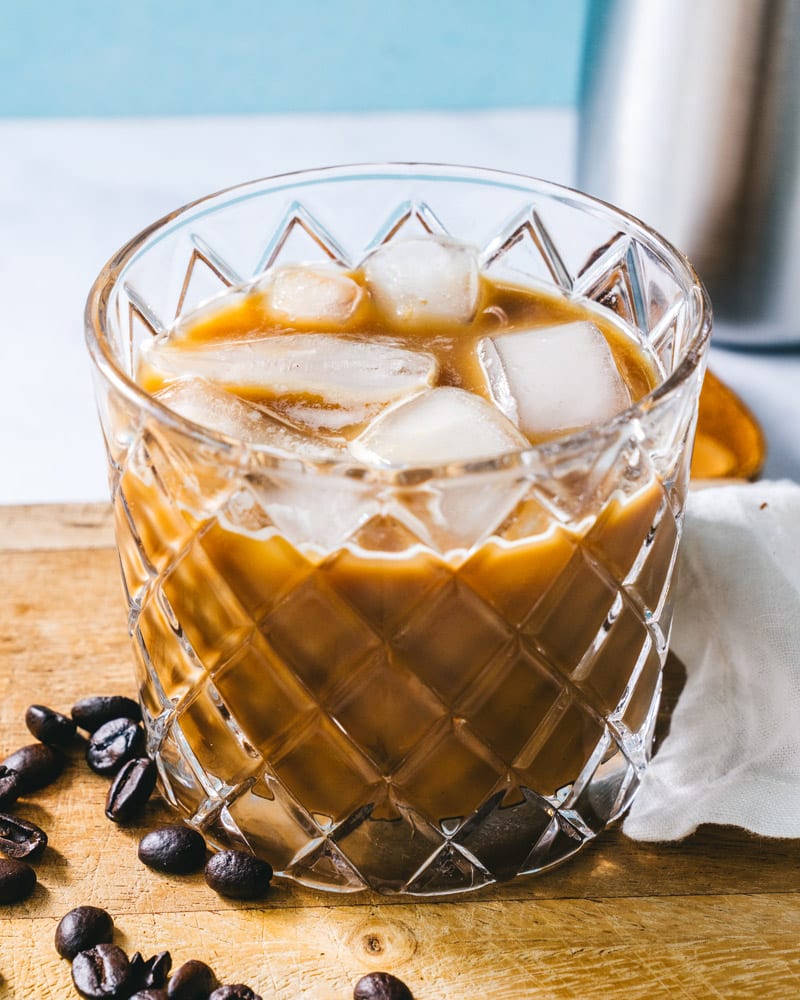 Iced Espresso in a textured glass with scattered coffee beans next to it