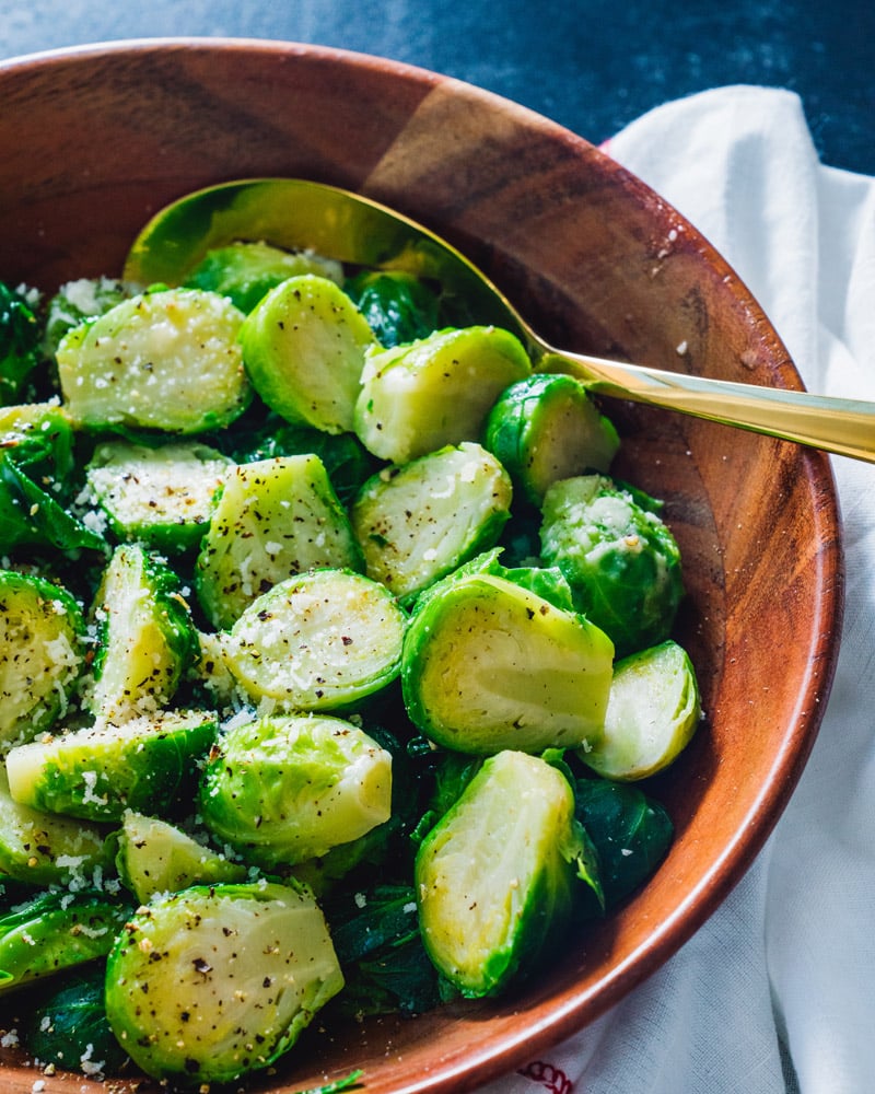 Boiled Brussels Sprout halves in a bowl with a utensil and covered in seasoning