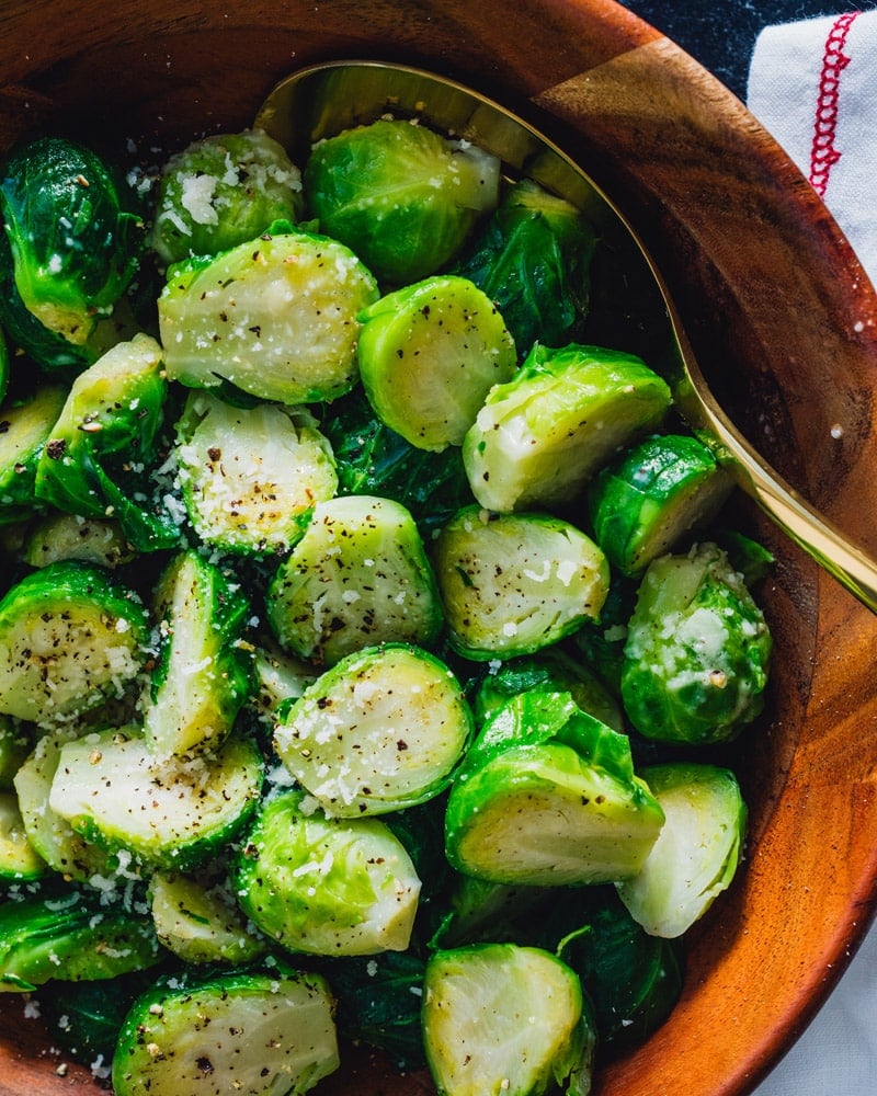 Boiled Brussels Sprout halves in a bowl with a utensil and covered in seasoning