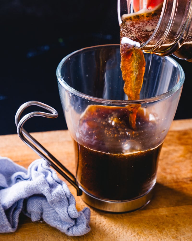 a cup of coffee in a glass cup with an interesting hook handle with coffee being poured into it