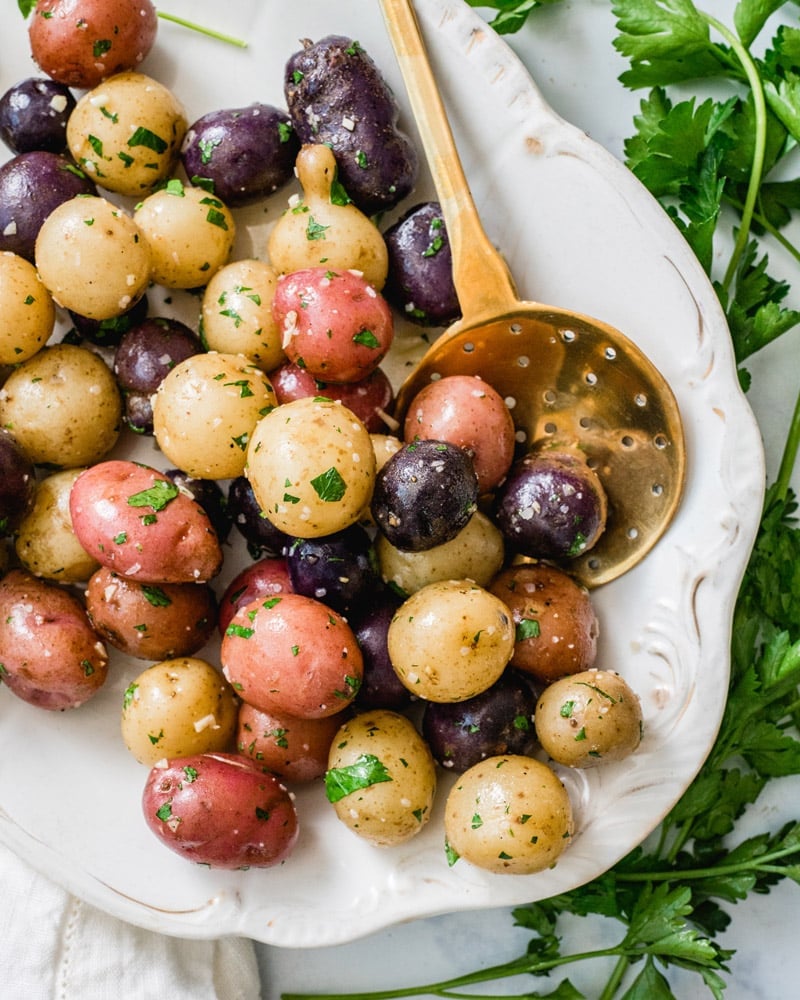 A medley of garlic steamed potatoes on a white plate, surrounded by parsley.