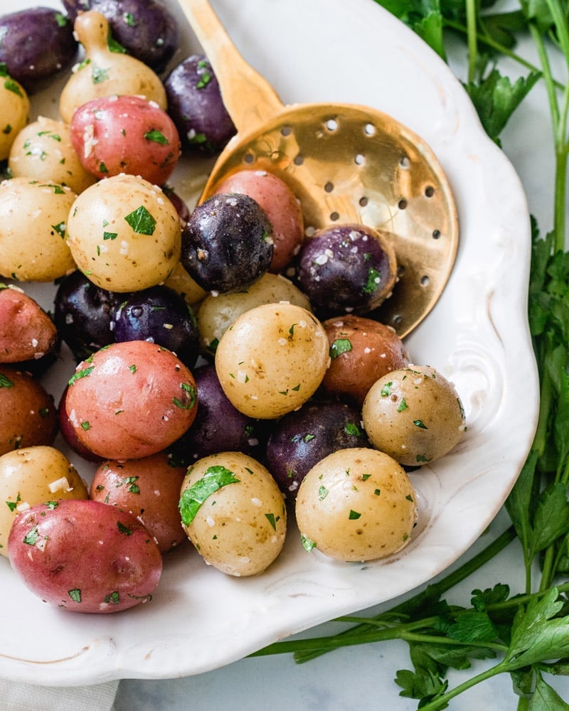 Garlic steamed potatoes, featuring a medley (purple, red, and yellow) on a white plate surrounded by parsley