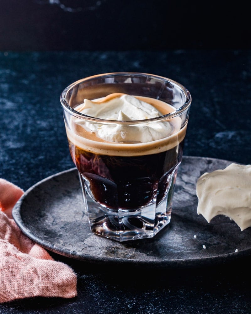 Espresso Con Panna in a short glass with a spoonful of cream in the background