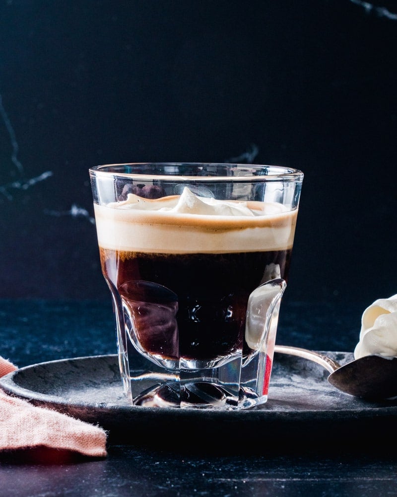 Espresso Con Panna in a short glass with a spoonful of cream in the background