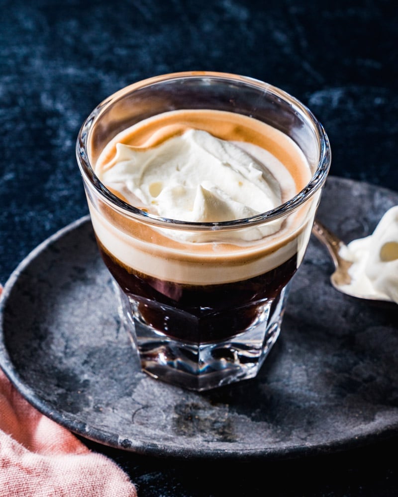 Espresso Con Panna in a short glass with a spoonful of cream in the background