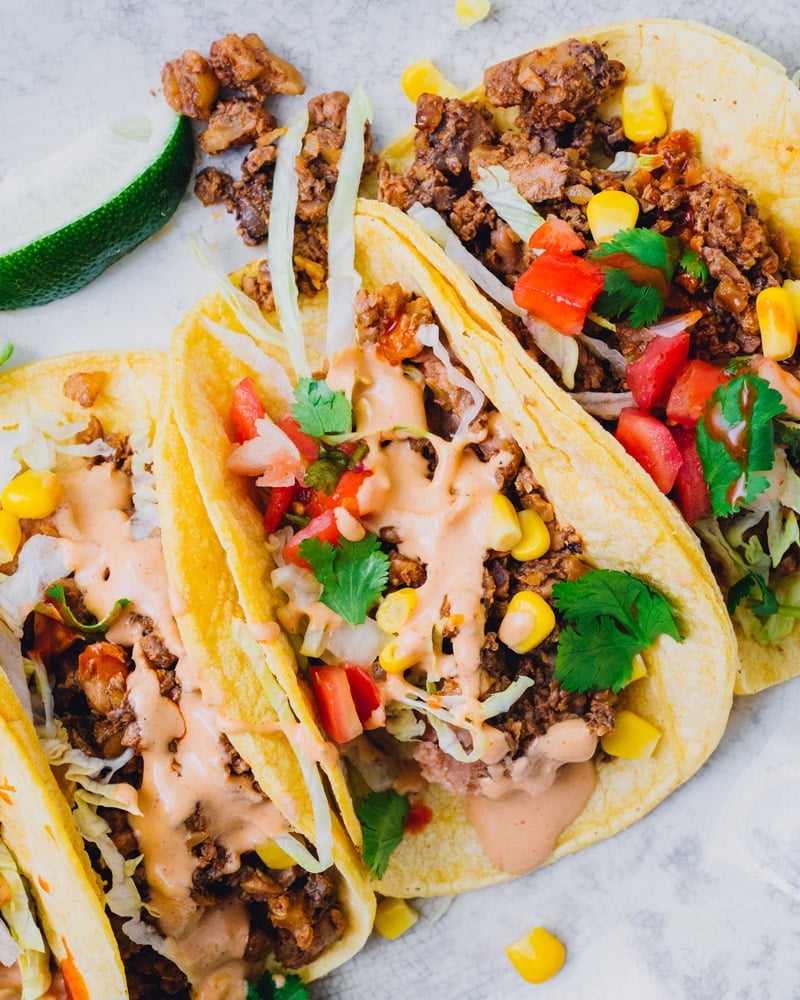 Three vegan tacos topped with pico, corn, and a zesty sauce