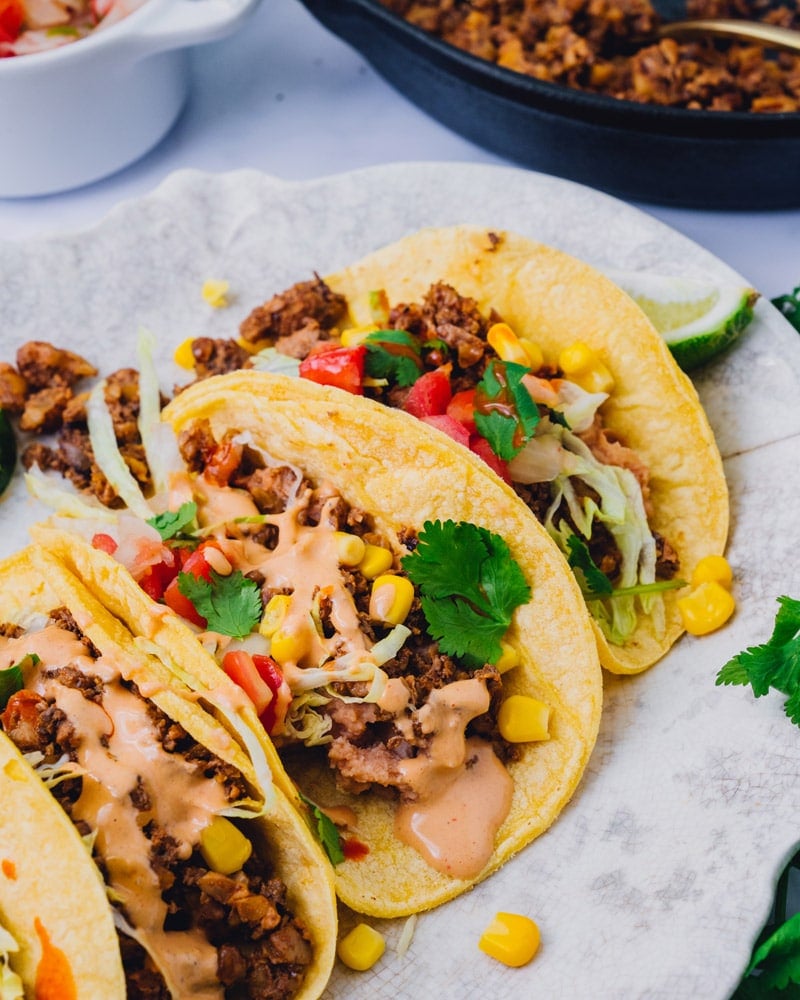 Three vegan tacos topped with pico, corn, and a zesty sauce