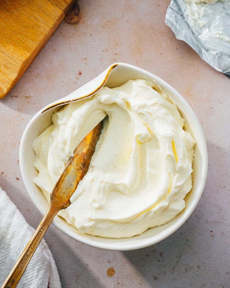 Whipped cream cheese in a uniquely shaped bowl, with a spreading knife dipped into it