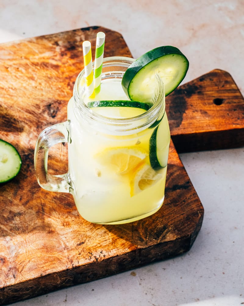 Cucumber Lemonade in a mason jar wtih a handle and two straws, garnished with lemons and cucumbers