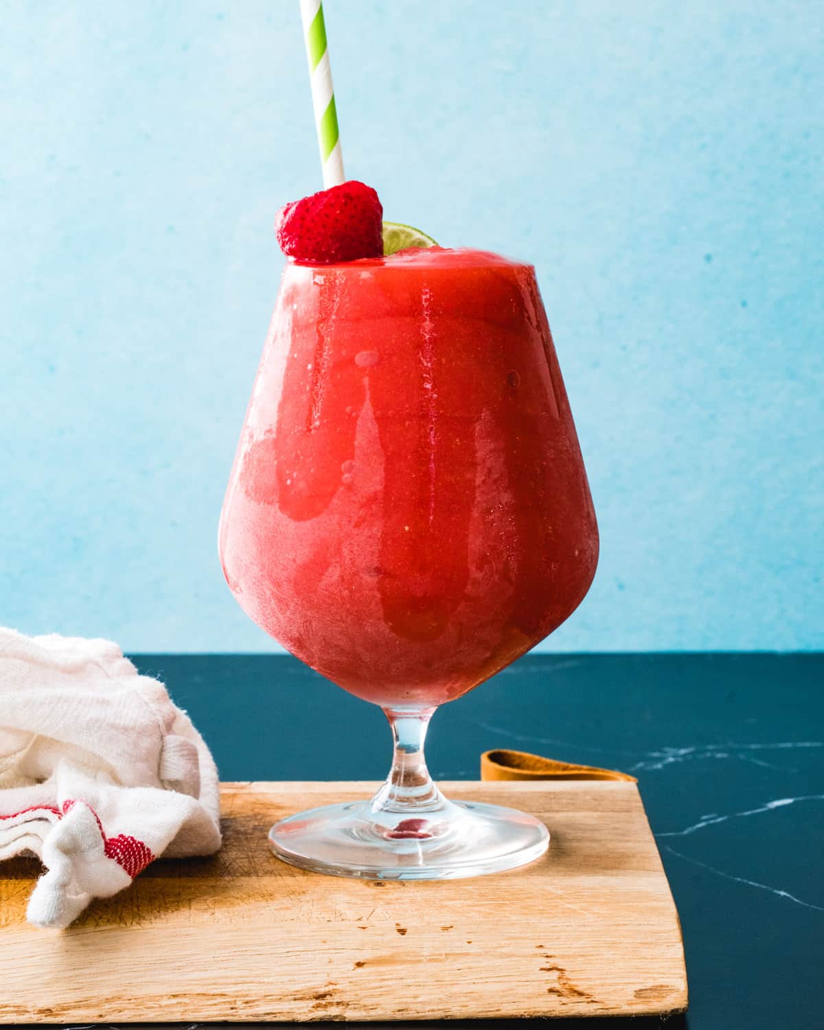Strawberry daiquiri recipe in glass with straw and strawberry garnish.