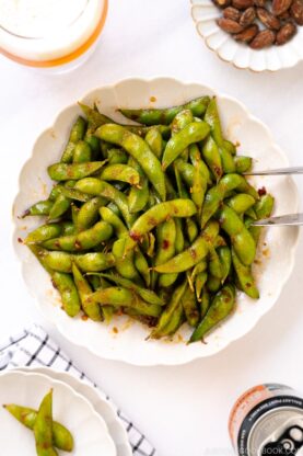A white ceramic plate containing spicy edamame.