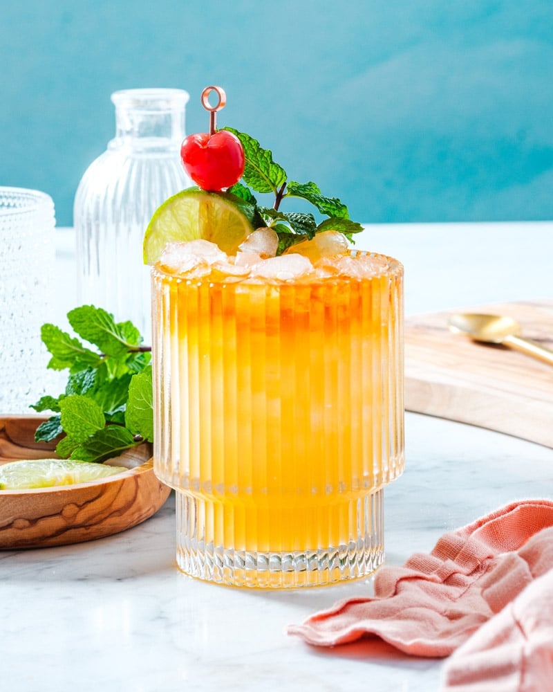Mai Tai drink in a short glass with ice and garnished with lime, cherry, and fresh mint leaves