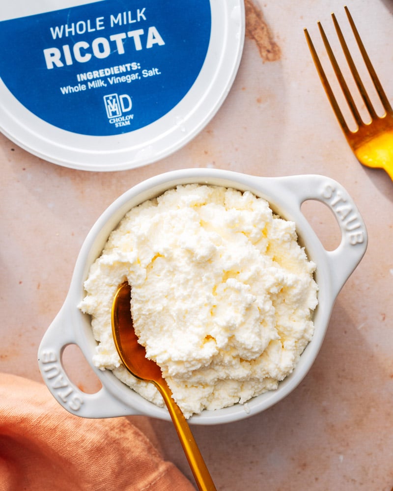 A container of "whole milk ricotta" sitting next to a white bowl of frozen ricotta