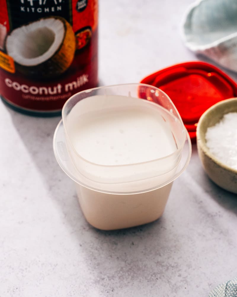A small container full of milk next to a can of Thai Kitchen coconut milk