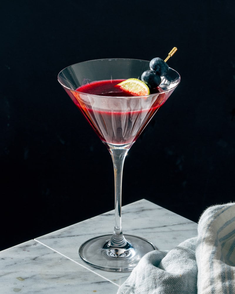 Blueberry martini in a cocktail glass, garnished with blueberry and lime