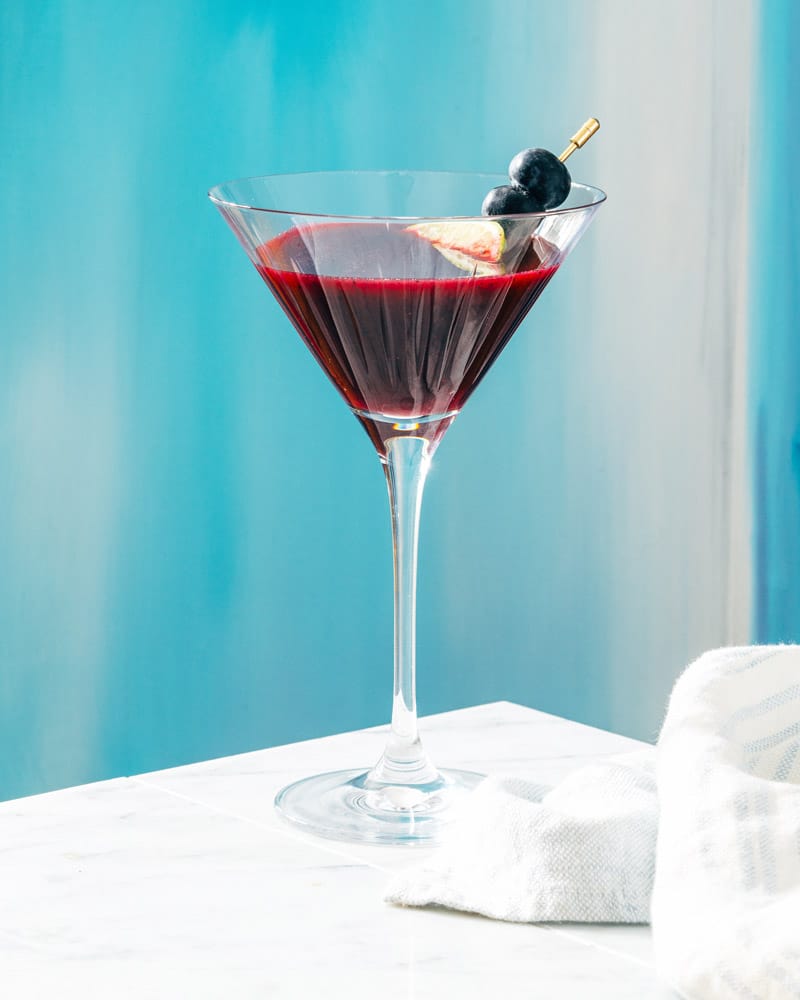 Blueberry martini in a cocktail glass, garnished with blueberry and lime
