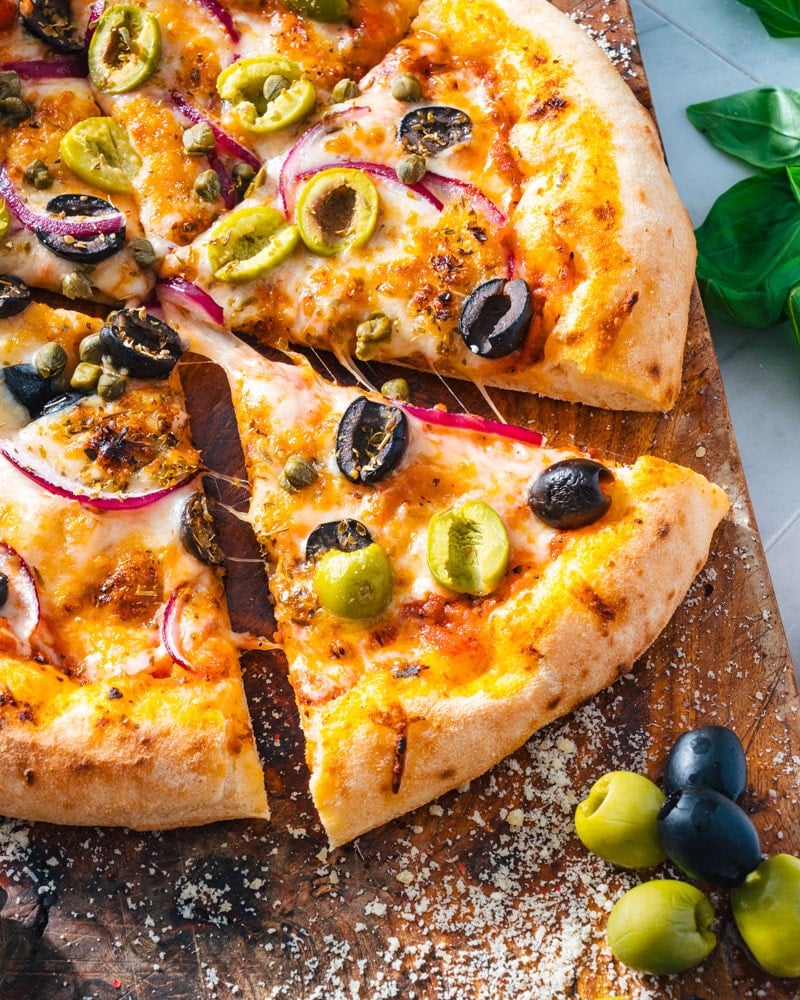 Olive Pizza on a cutting board with red onion, capers, and green and black olives