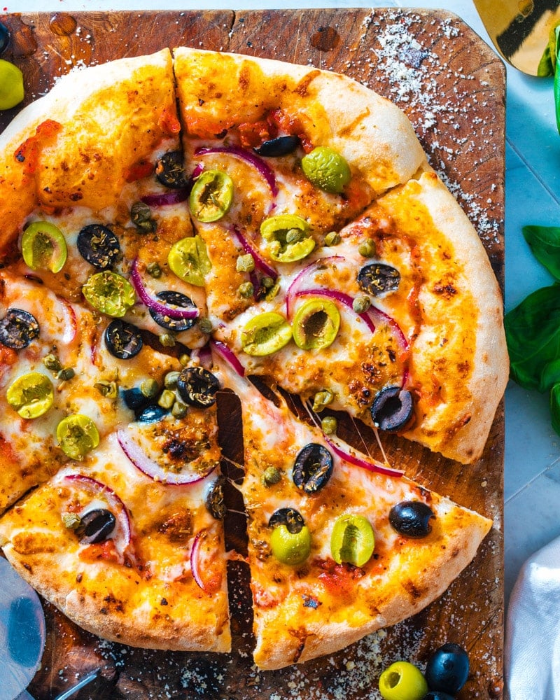 Olive Pizza on a cutting board with red onion, capers, and green and black olives