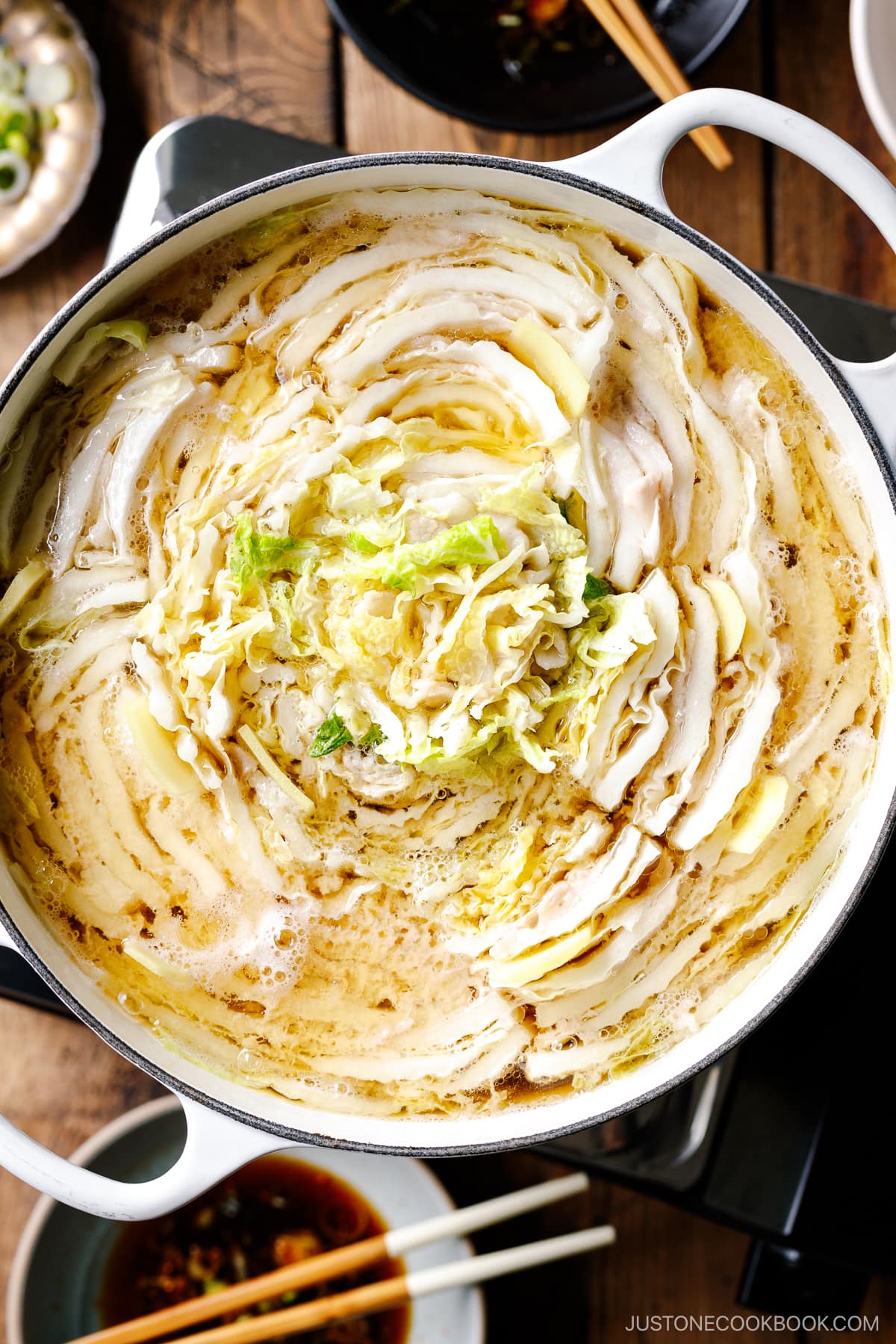 A Le Creuset pot containing Mille-Feuille Nabe, which is a hot pot dish with layers of pork belly slices and napa cabbage slices in a dashi broth.