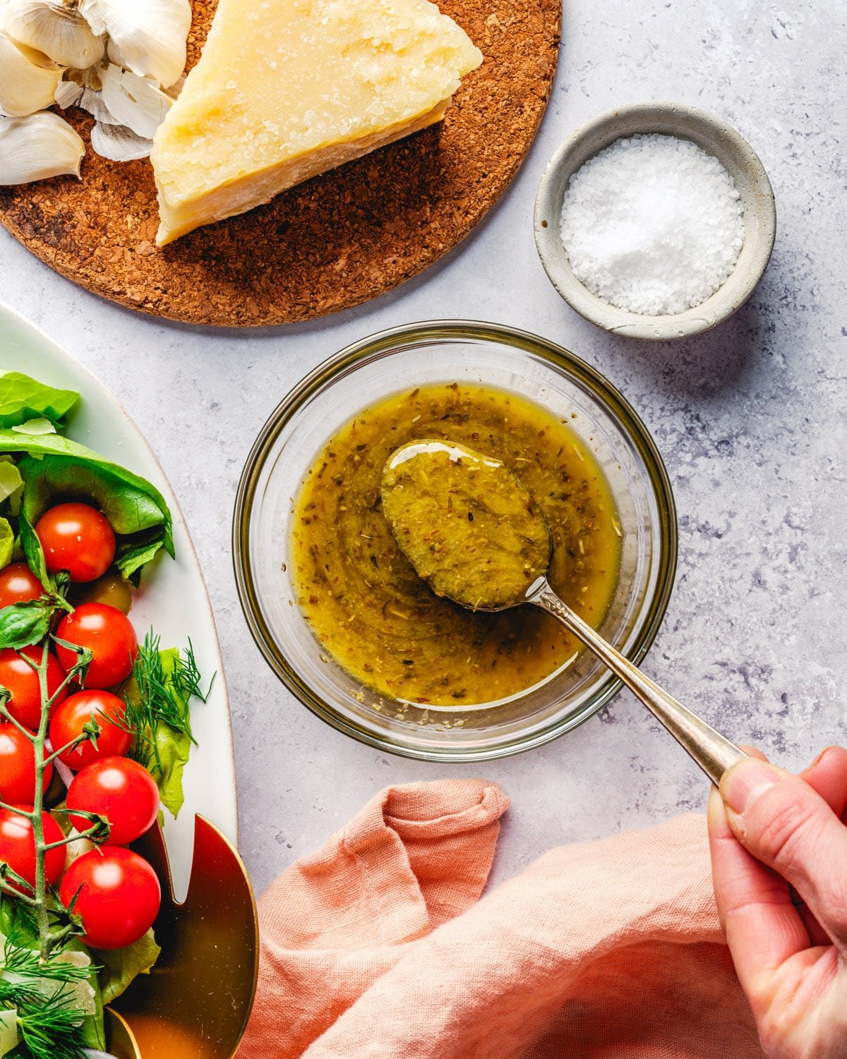 Italian Dressing in bowl with spoon, salad, and Parmesan cheese.