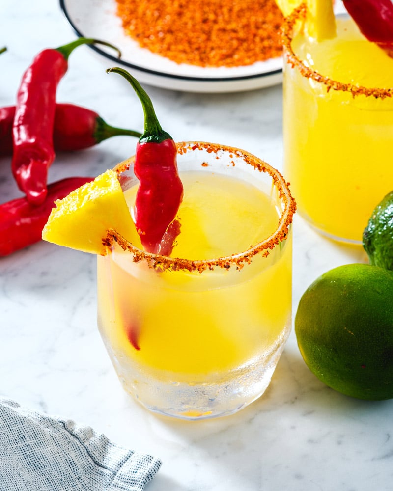 Spicy Pineapple Margarita  in a glass with Tajin rim and spicy pepper garnish