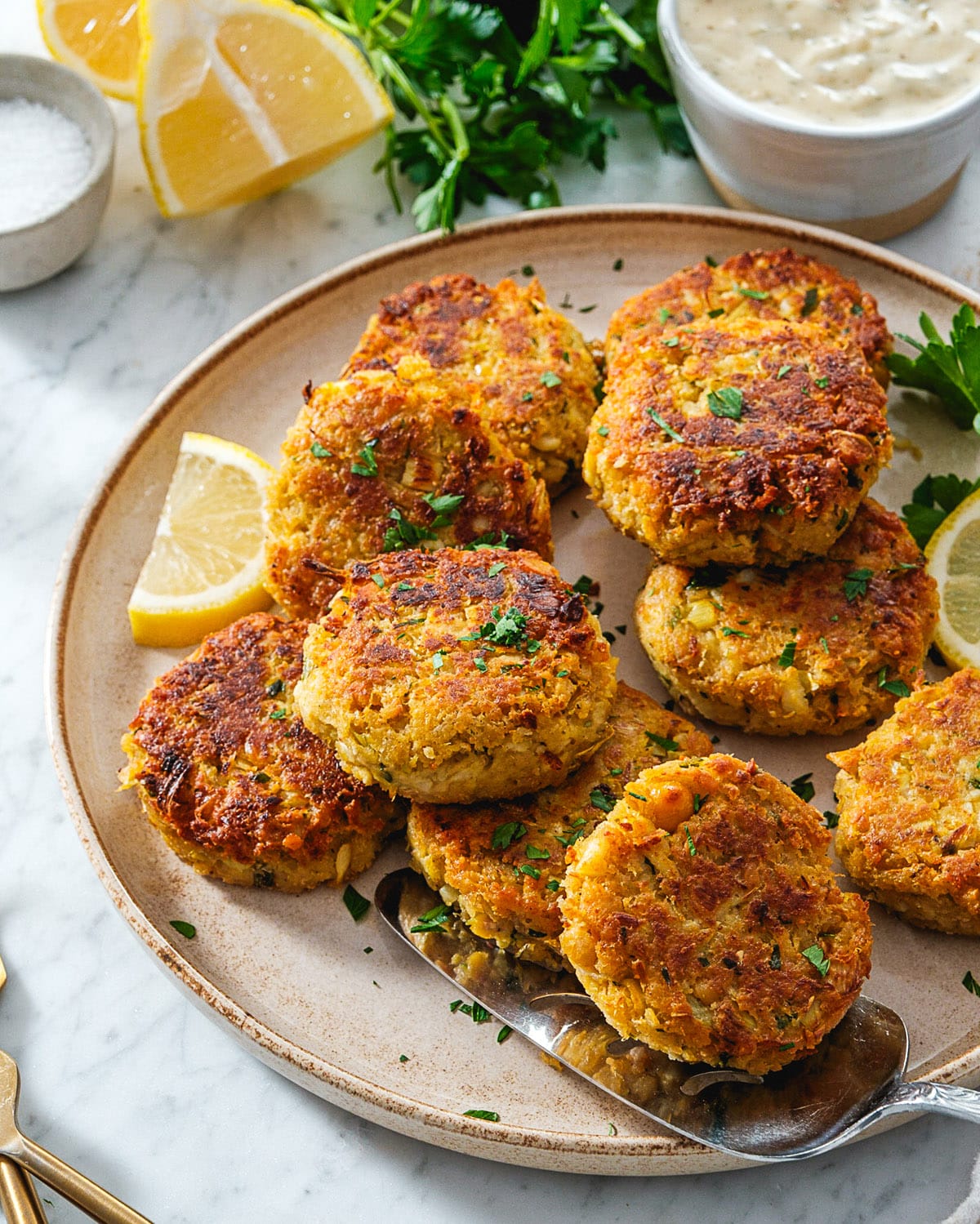 Vegan Crab Cakes on a plate with lemon wedges and a side bowl of Vegan Tartar Sauce