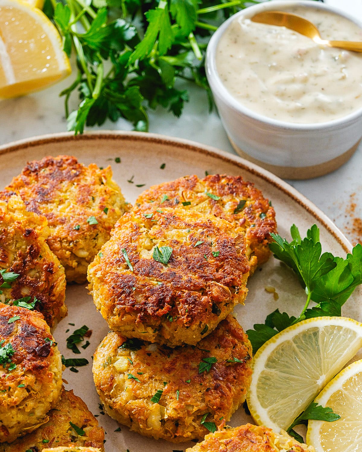 Vegan Crab Cakes on a plate with lemon wedges and a side bowl of Vegan Tartar Sauce