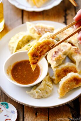 A round plate containing Japanese pan-fried dumplings, Napa Cabbage Gyoza, served with a savory miso dumpling sauce.