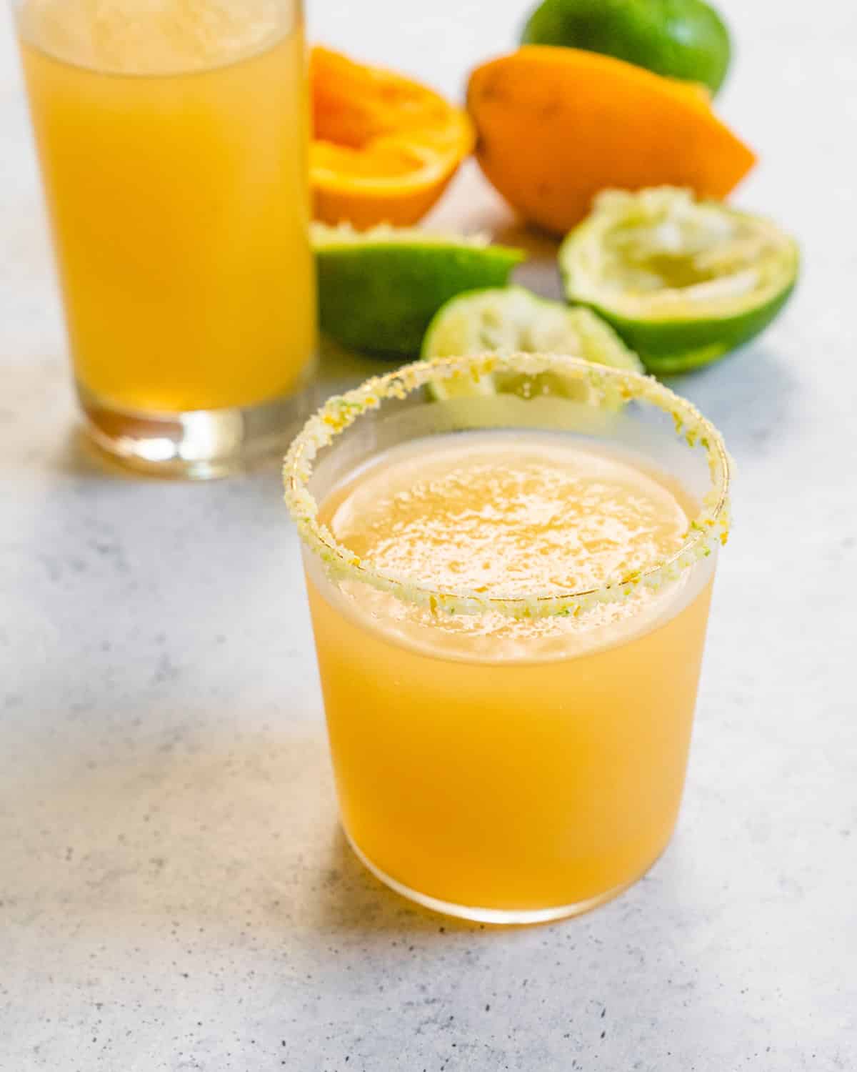 Margarita salt on rim of margarita glass with squeezed limes and lemons in the background