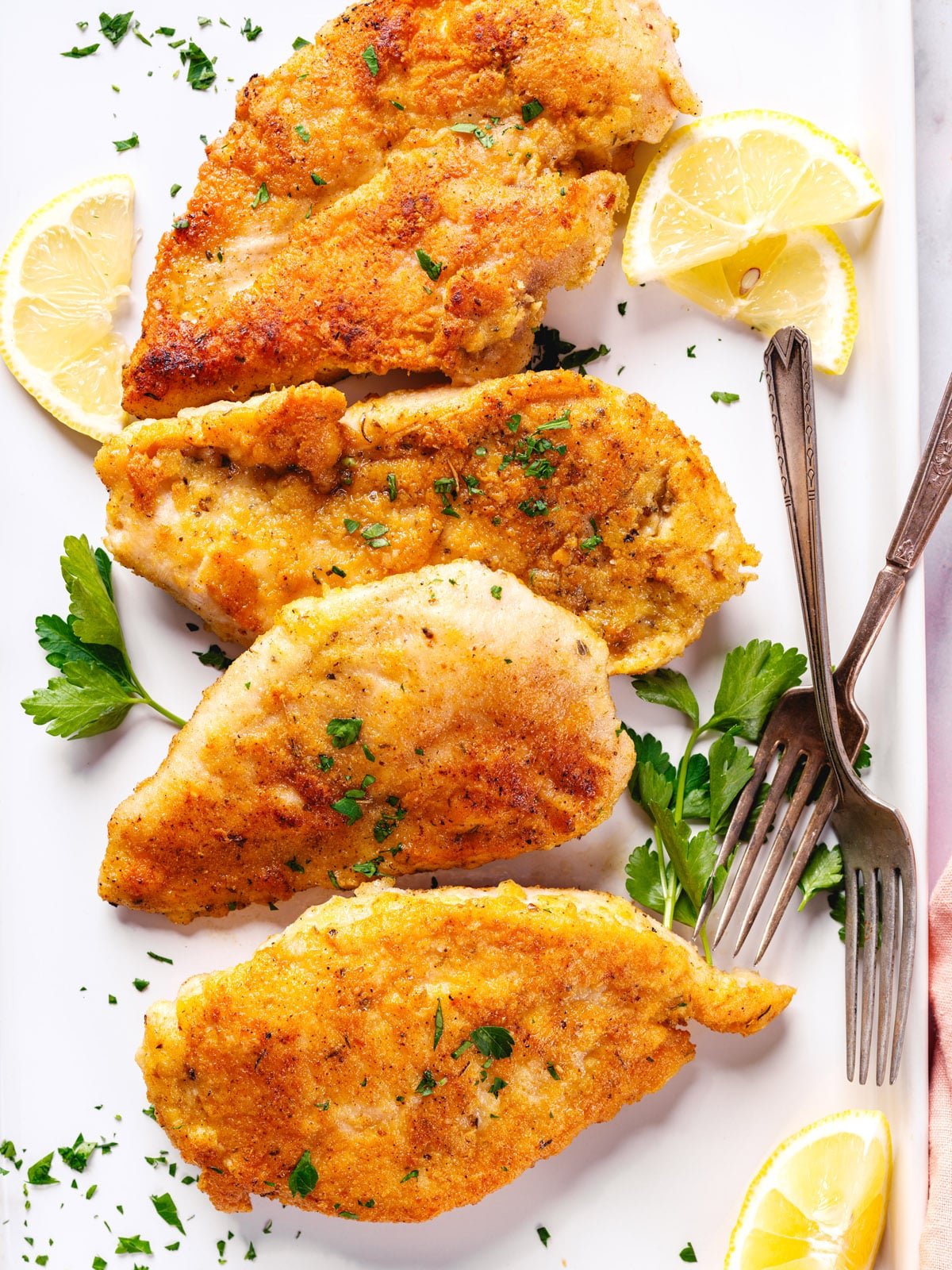 Parmesan crusted chicken breast on a platter with lemon wedges