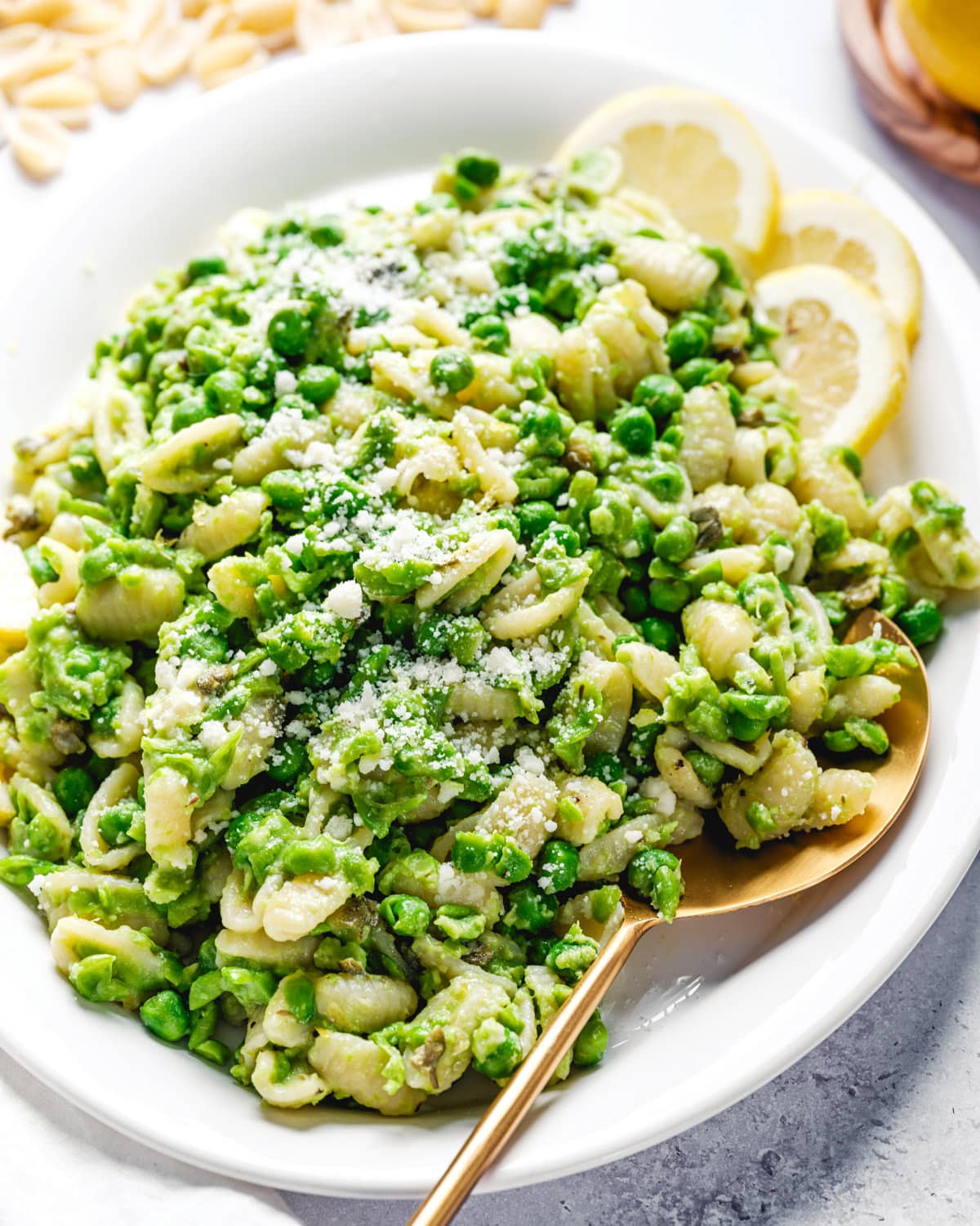 Pasta with Peas on a plate with serving spoon and lemon slices.