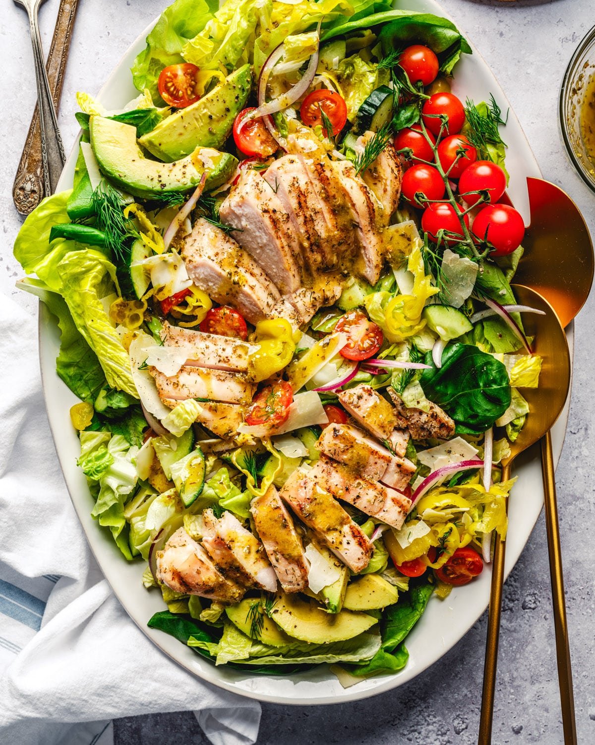 Grilled chicken salad on plate with serving spoons. 