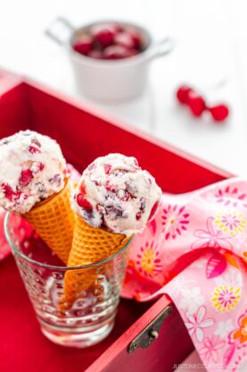 A glass cup containing cherry ice cream on a waffle cone.