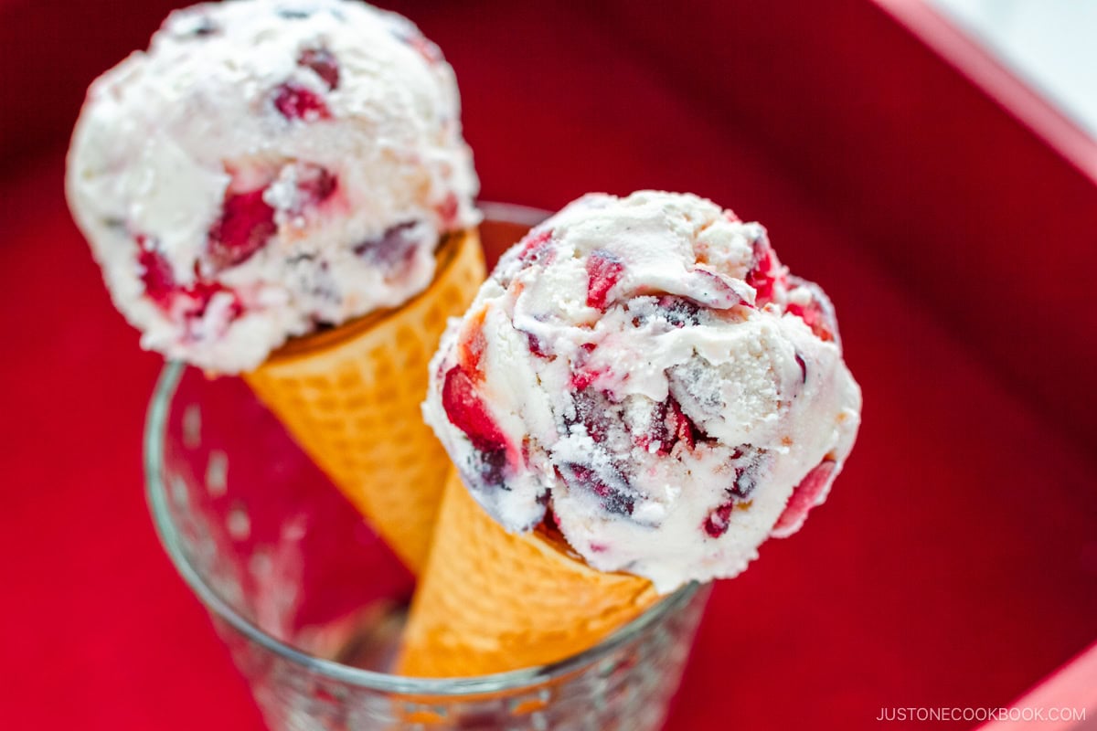 A glass cup containing cherry ice cream on a waffle cone.