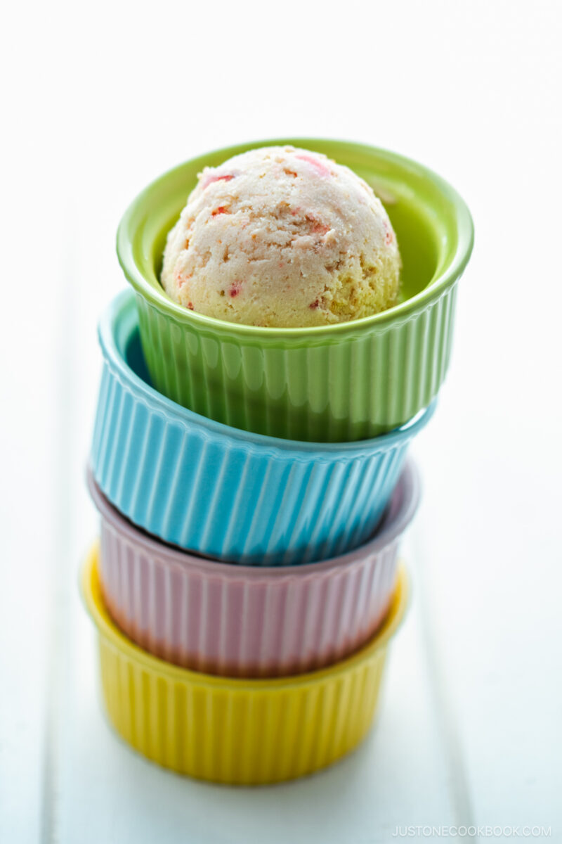 Colorful ramekins piling up on top of each other and a green one containing containing a scoop of strawberry ice cream.
