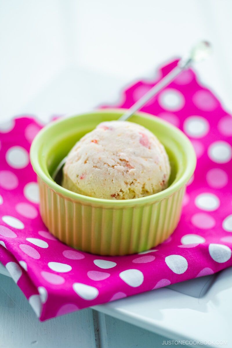 A green ramekin containing a scoop of strawberry ice cream.